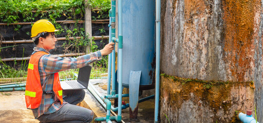 Engineer working in drinking water factory using a laptop computer to check water management system and boiler water pipe  outside the factory