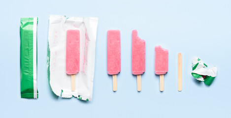 Pink popsicle ice cream on wooden stick at different states of consumption life cycle on blue background top view flat lay