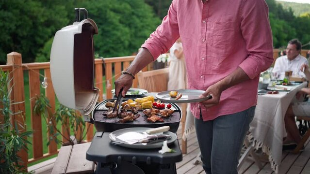 Man grilling ribs and vegetable on grill during family summer garden party, close-up