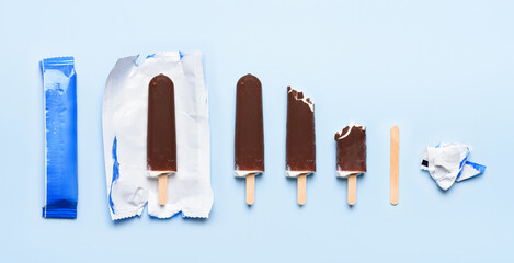 Chocolate covered ice cream on wooden stick at different states of consumption life cycle on blue...