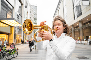 Young caucasian long-haired blond man in white shirt playing funky jazz on golden trumpet with...
