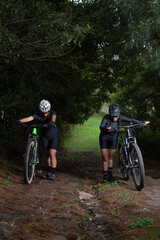 Fototapeta premium Two sporty women pushing their bikes up a difficult mountain trail