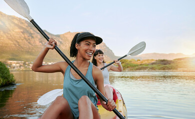 Two smiling friends kayaking on a lake together during summer break. Smiling and happy playful...