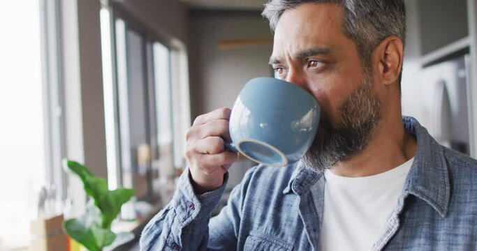 Biracial man drinking mug of coffee and thinking in kitchen alone