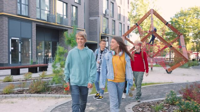 Joyful young teens friends speaking while walking in city holding in hands skateboards. Stylish boys and girls skaters going to skate park. Skateboarding, youth culture, leisure activity concept