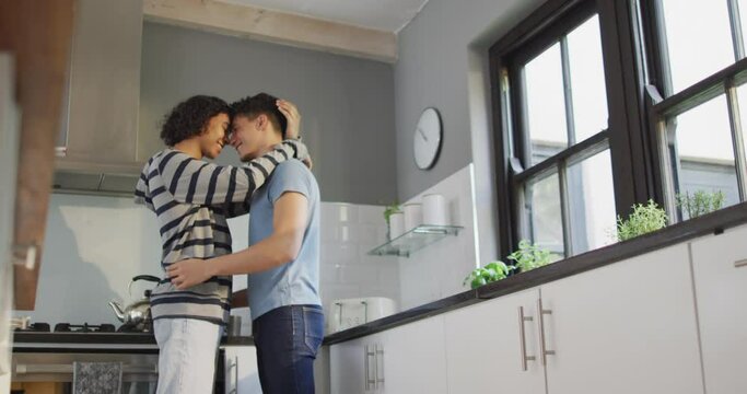 Happy diverse male couple smiling and dancing together in kitchen