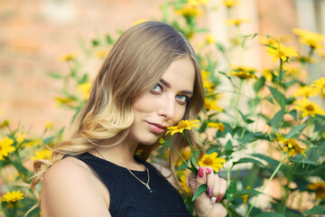 Naklejka premium Young beautiful woman in a black dress enjoys the smell of blooming yellow flowers. Outdoor portrait in blooming spring park