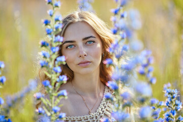 Beautiful young woman in blue flowers outdoors. Échium vulgáre. Boho style clothing. Looking at camera. (Selective DOF)