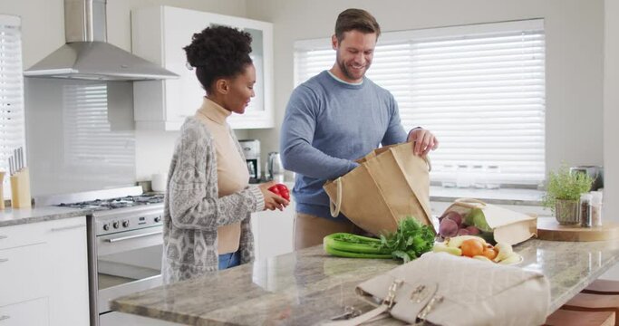 Video Of Happy Diverse Couple Unpacking Groceries In Kitchen