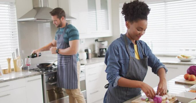 Video of happy diverse couple preparing meal, cutting vegetables in kitchen