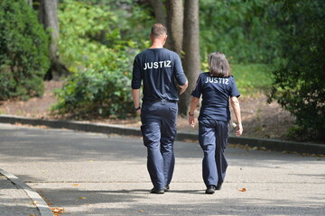 A female and a male german correctional officer in her uniforms walking through a park in...