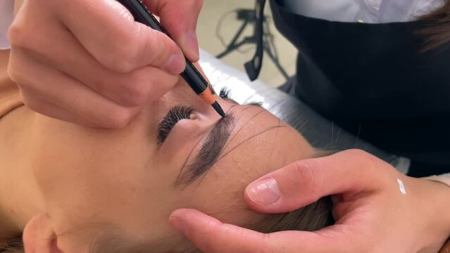 Permanent makeup eyebrow close-up view. Master draws a contour of eyebrows