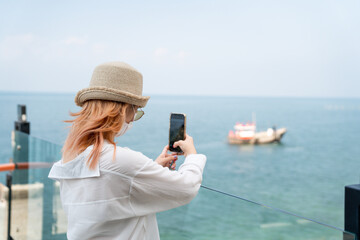 Young female taking a photo of the sea with cellphone, smartphone, travel alone