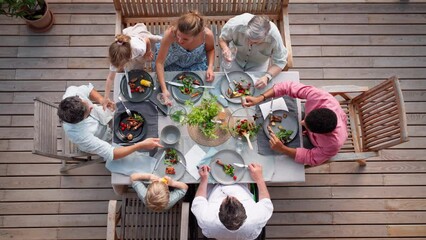 Top view of 3 generations family eating at barbecue party dinner on patio, people sitting at table on patio with grill.