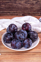 Black plums on wood background. Pile of black plums on a white serving plate. close up