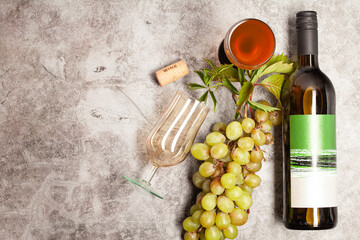 White wine bottle with bunch of grapes, glass on a dark background, top view.