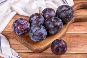 Black plum on wood background. A pile of black plums on a wood serving dish. close up