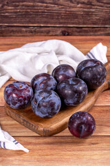 Black plum on wood background. A pile of black plums on a wood serving dish. close up