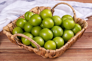 Green plum on wood background. A pile of green plums in a basket. close up