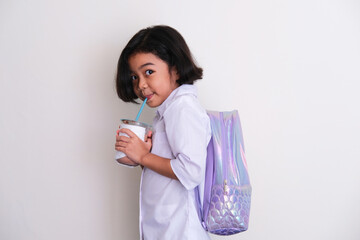 Side view of Asian kid wearing school uniform and backpack drink a cup of cold chocolate milk