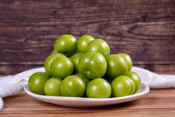 Green plum on wood background. Pile of green plums on a white serving plate. close up