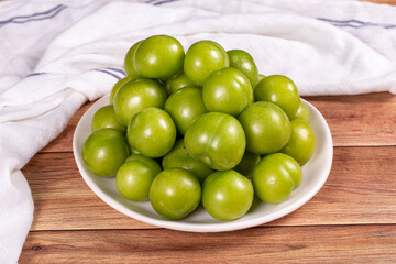 Green plum on wood background. Pile of green plums on a white serving plate. close up