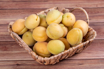 Naklejka na ściany i meble Apricots on wood background. A pile of fresh apricots in a basket. close up