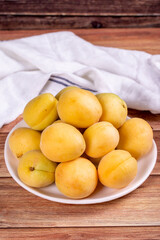 Naklejka na ściany i meble Apricots on wood background. Pile of fresh apricots in a white plate. close up