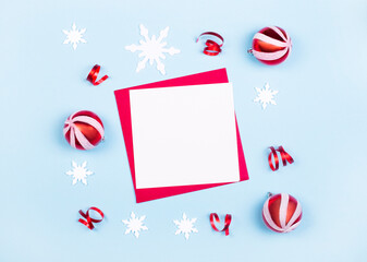 Christmas composition. Blank paper, Christmas red balls, white snowflakes on a light blue background. Flat lay, top view, copy space. Holiday card with place to insert text
