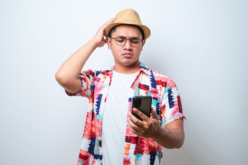 Portrait of unhappy Asian man in casual beach shirt holding mobile phone with sad expression on face while scratching his head.