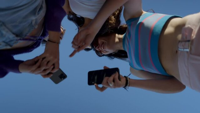 Happy girls in sunglasses use phones and talk, close view from below