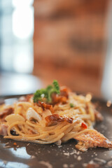 Tasty appetizing classic italian spaghetti pasta with creamy sauce, cheese parmesan and basil on plate on dark table at cafe restuarant. 