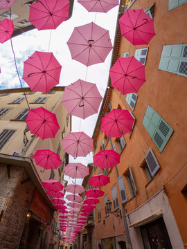 Grasse,  France,  October 3, 2021: Suspended pink umbrellas in the historic center of Grasse, celebrating the Rose Expo.  Elements of architecture of Grasse with colored umbrellas between houses.