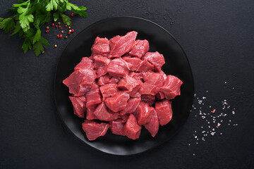 Raw chopped beef meat. Raw organic meat beef or lamb, spices, herbs on black plate on dark grey concrete background. Goulash. Raw uncooked meat. Meat with blood. Top view with copy space.