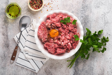 Raw minced meat. Ground meat beef, pork or lamb spices, herbs and eggs on white plate on light grey concrete background. Fresh minced meat ready for cooking. Food cooking background. Top view.