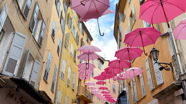 Grasse,  France,  October 3, 2021: Suspended pink umbrellas in the historic center of Grasse, celebrating the Rose Expo.  Elements of architecture of Grasse with colored umbrellas between houses.