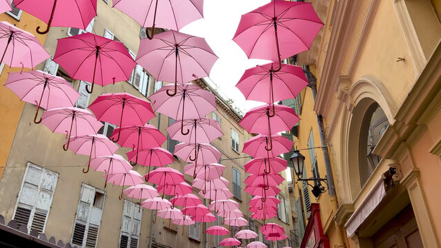 Suspended pink umbrellas in the historic center of Grasse, celebrating the Rose Expo in Provence-Alpes-C&ocirc;te d'Azur, France. Elements of architecture of Grasse with colored umbrellas between houses.