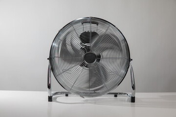 Silver metal floor ventilation fan on white floor at home or business with grey wall.