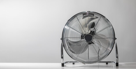 Silver metal floor ventilation fan on white floor at home or business with grey wall.