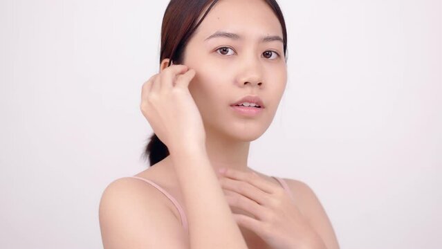 Slow motion of Asian girl with natural make up looking to camera and patting her face gently on white background.