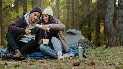 Young couple in love travelers sits in nature resting drinking tea from thermos enjoy hot drink...