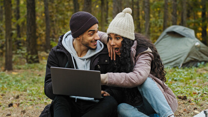 Young happy couple in love tourists sit outdoors in campsite look at laptop screen choose place to...