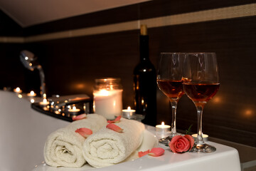 Glasses of wine, towels and rose on tub in bathroom. Romantic atmosphere