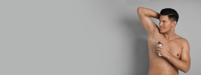 Handsome man applying deodorant to armpit on grey background, space for text. Banner design