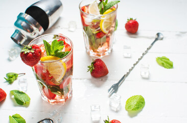 Summer refreshing mojito cocktail with strawberry, mint and lime with shaker for whipping drinks on white wooden table
