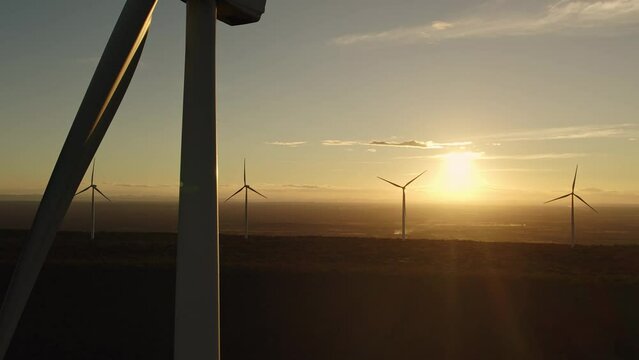 Aerial going up shot with golden Sunset view with wind turbine towers in the background and a big one in the close up shot, Alternative energy source