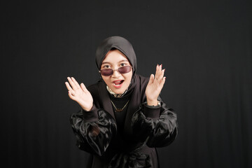 Happy young Asian Muslim woman wearing glasses isolated on black background.