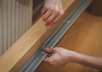 Obraz premium The hands of a caucasian young man twisting a screw with a screwdriver connecting a metal part to a wooden bed