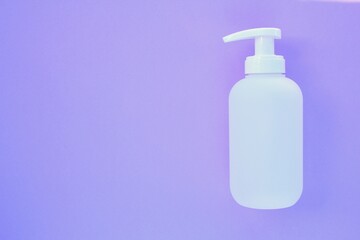 White unbranded plastic dispenser pump bottle on purple background with copy space for text. Cosmetic package mockup, liquid soap flacon, hand sanitizer without label, shampoo organic spa, shower gel