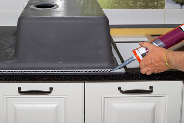 Applying black sanitary sealant with a nail gun to the edge of the kitchen sink. Installing a sink...
